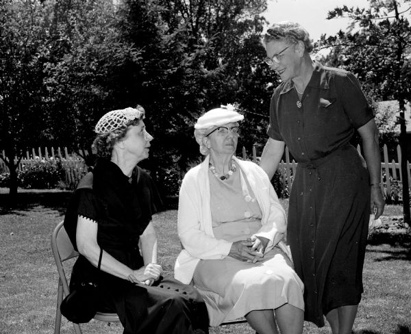 Vera Browne and Esther Piepenburg enjoy a sunny day seated outside while attending the Madison Council of Church Women's afternoon tea. Standing at right is hostess Loretta Iler of 4547 Winnequah Road.