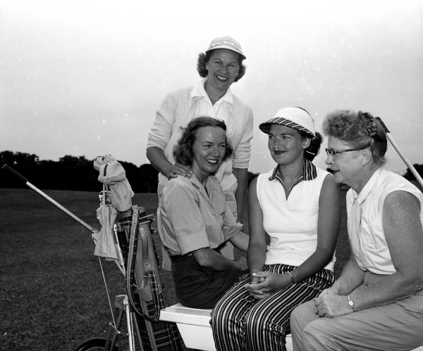 Four women in golfing clothes posing by a pull golf cart. Standing is Alphida Voight; seated are Dorothy Martin, Mildred Wellman, and Ruth Ellis.