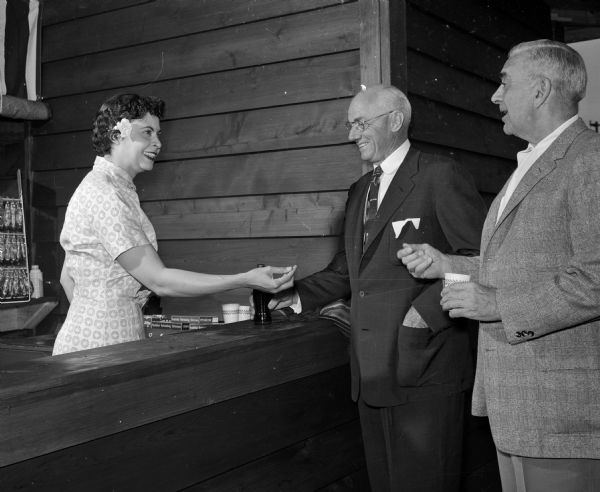 Mrs. Frances Parrish of Louisville, Kentucky volunteers at the opening of the Green Ram theater near Baraboo. She is serving soft drinks to Reid M. Bergh, left, and Willard A. Lowe, both of Madison.