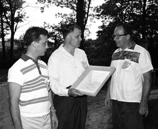 A plaque bearing the title "Bohemian Brigade" was presented to Karl H. Fauerbach for his support of the Press Club at a picnic on the grounds of the Fauerbach estate, located north of Madison. The name is in honor of the newspapermen who covered the Civil War. Richard Harron, Carl Guell (club president), and Ed Barris inspect the plaque. Harron and Barris are Fauerbach salesmen.