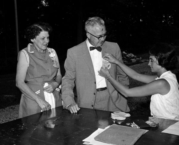 Mr. and Mrs. Arthur Jorgensen of Columbus are assisted with their "beer stein" name tags by Helen Klieforth, treasurer of the Press club at a picnic on the grounds of the Fauerbach estate, located north of Madison.