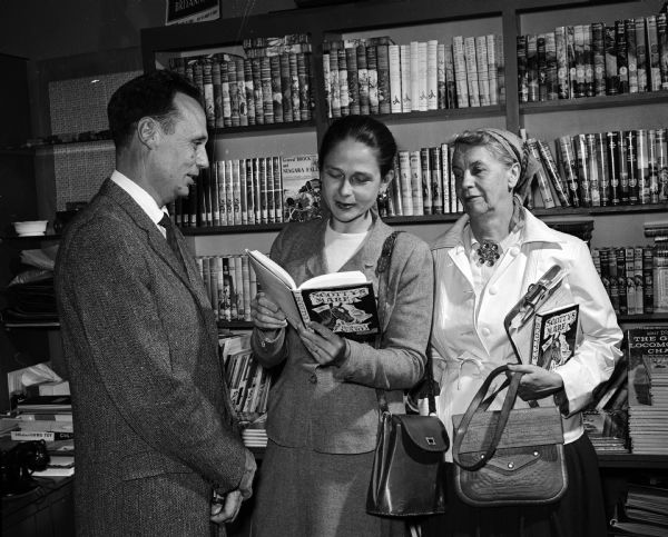 Robert Gard, University of Wisconsin speech professor, is standing beside Elizabeth Bardwell and Harriet Bunn at an autographing tea at Graham's Book and Stationary Store, 3238 University Avenue. Bardwell is looking at a children's book, "Scotty's Mare," illustrated by Aaron Bohrod, University of Wisconsin artist in residence.
