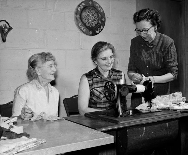 Members of the De Porres Guild make preparations for the upcoming bazaar. Proceeds will benefit the Blessed Martin Guild which conducts social, recreational, cultural, and religious programs at Blessed Martin House. From left, Kathryn Murphy, Aileen Weber, and Marcia Etteldorf (chairman of the "white elephant" booth) work at a sewing machine.