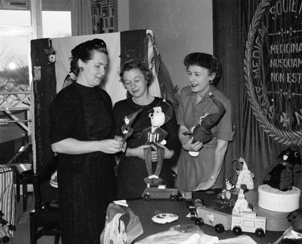 Three women attend an event to display Dane County Medical Society Women's Auxiliary projects. They are, from left, Mrs. A.P. Schoenenberger, auxiliary president; Mrs. G.T. Schulz, Union Grove; and Mrs. A.J. Baumann, Milwaukee, state auxiliary president. They are viewing hand-made toys made by Dane County handicapped persons.