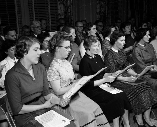 Members of the Philharmonic Chorus hold a reception in Esther Hall of the YWCA.  Eleanor Barschall (left), Mrs. A.G. Grover, and Mary Ylitalo rehearse a song.