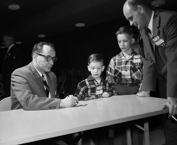Marvin Reimann, left, makes out a registration tag with Loren Wedel, right, and his two sons, Douglas and Billy, while attending the father-son banquet at Immanuel Luther church.
