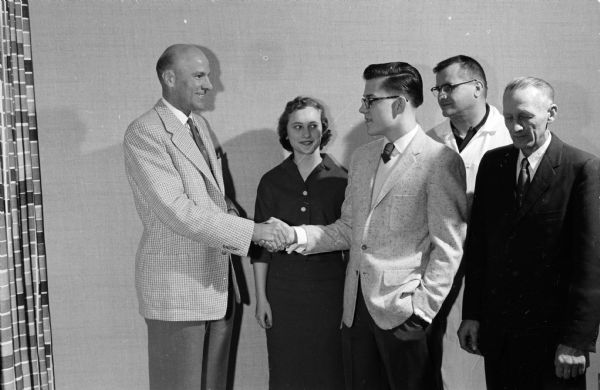 Oscar G. Mayer, Jr. presenting scholarship certificates to two Madison High School students. Left to right: Oscar Mayer, Jr. and recipients Barbara Jean Hoppe and John Hermanson. Leslie Hoppe and Robert Hermanson, Oscar Mayer employees and fathers of the winners, look on.
