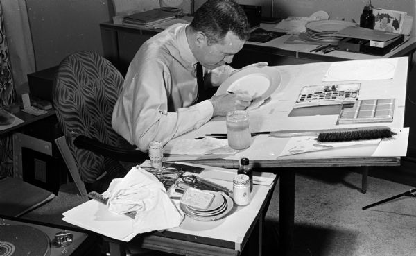 Portrait of John Eustice, a designer of china patterns, at work in his studio. A graduate of University of Wisconsin, and New York State College of Ceramics, John specializes in the art of hand-decorated fine china. One of his designs was chosen for use in the White House by Mrs. Eisenhower.