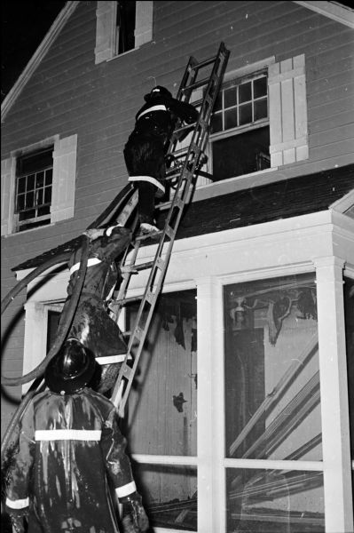 Two firemen hold a ladder while going up a ladder to fight a fire that destroyed the interior of the Graham Johnson residence at 22 Burrows Road in Maple Bluff.