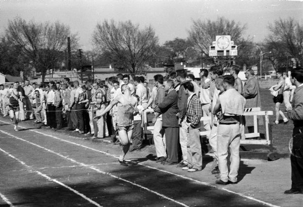 A track runner with his head tilted back wins a race. The runner, Jack Stoltz, is shown completing the 880 yard leg of the sprint medley for East High School's relay team victory. Stolz was also a former Richland Center letterman.