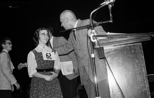 Carol Fellows, a 14-year-old girl from Genoa City, is shown at the moment she was declared Badger State Spelling Bee champion. She outspelled 62 other city and county champions. Congratulating her is J.W. (Bill) Clark, master pronouncer, who had to pronounce 3 1/2 hours until a champion was named.