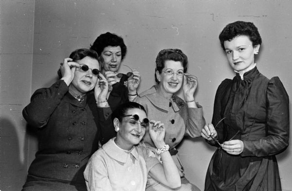 Members of the Madison Auxiliary of the Wisconsin Optometric Association will present the skit "The Historic Spectacle," showing the changes in eyeglasses through the years at the annual banquet in Milwaukee. Mrs. T.O. Wipperfurth, right, is the public relations director. Mrs. Warren Bohlinger seated in the chair is the state historian. Anita Strobel left is the state president. Mrs. Vernon Denner and Leona Roman, right, model some of the glasses.