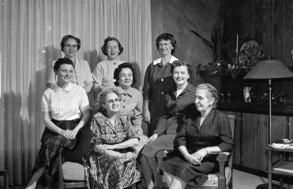 Group portrait of eight Madison area Optimist Club wives assisting in plans for a upcoming district Optimist convention. Left to right, front row: Iola Reppen and Bessie Starr. Middle row: Maribeth Olson, Mrs. Harry P. Stoll, and Mrs. Raymond Lemke. Back row: Mrs. Ray Wolf, Verona; Mrs. Wallace Smith, Middleton and Mrs. William Newhouse.