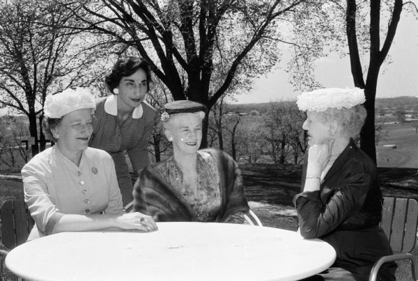 A fashion show with models from various Madison credit unions is presented at a luncheon given at the Blackhawk Country Club for the wives who accompanied their husbands to the annual meeting of the Credit Union National Assn. (CUNA), and its affiliated organizations. Seated at the table are, left to right, Mrs. Louis Bonderefsky, New York City; Mrs. Paul L. Higley, Berkeley, Calif.; and Mrs. A.P. Quinton, Hamilton, Ontario, Canada. Standing is Miss Emily Spencer of New Orleans, La.