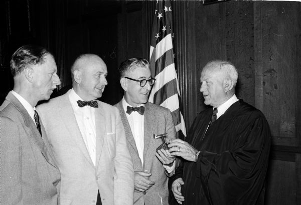 Federal Judge Patrick T. Stone receives a spinning reel as a gift to mark his 25th anniversary on the federal bench. Judge Stone is standing at right, and members of the presentation committee include, from left to right: George Schlotthauer, Lyall Beggs, and John Harrington.
