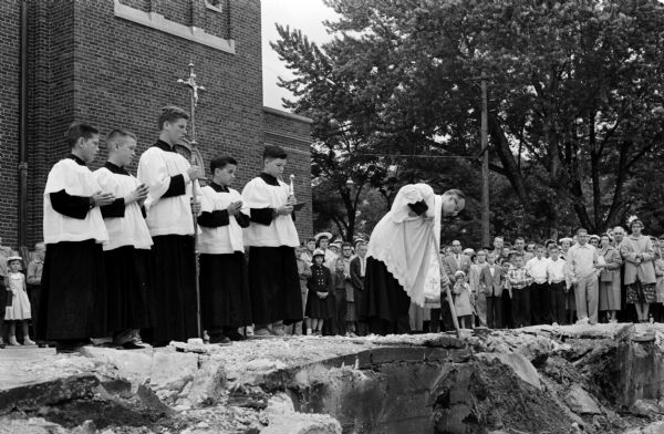 Rev. Louis Scheuring, pastor of St. James' Catholic Church, breaking ground for the new school after blessing the ground. Five altar boys assist Fr. Scheuring. From left to right are Michael Annen, Peter Dottl, Roy Skalaski, and David Keidel.