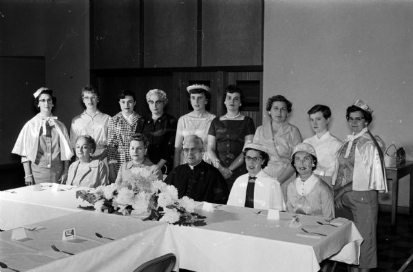 View of an installation ceremony at Our Lady Queen of Peace Court No. 597, Women's Catholic Order of Foresters. Seated left to right are Angeline VanDe Walker, Marion Racine, Monsignor Francis McDonnell, Helen Greenslet, chief ranger and Patricia Bruckner. Standing from left to right: Katherine Goetz, senior conductor, Kathleen Hensen, Kay Kurth, Dorothy Porter, Dolores Goldsmith, Edith Gallagher, Avis Joyce, Mary O'Keefe, and Mrs. Robert Graves, Junior Conductor.