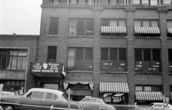 Exterior view of the front side of the Madison Newspapers, Inc. building at 115 South Carroll Street. The Wisconsin State Journal offices are on the 3rd floor and The Capitol Times offices are on the 2nd floor. Four stories of the building and three parked cars are visible.