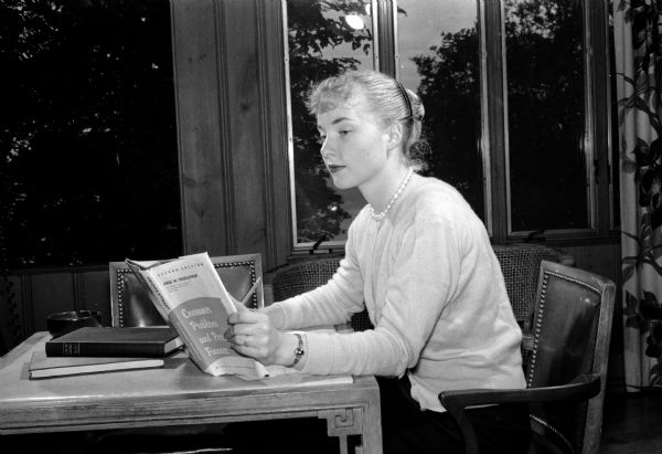 Co-ed seated at table by windows studying a book. The original caption states: "Sue Carolyn Renk received a B.S. degree with honors on June 16 in home economics education education. She is shown as she studies for final examinations at the Alpha Phi house, her sorority. She hopes to get a job as a home economist with a Florida utility corporation."