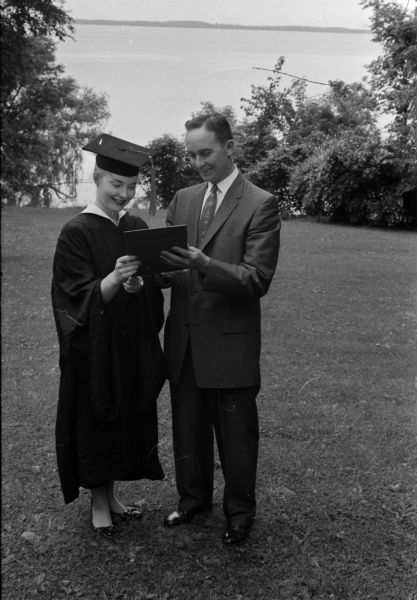 Sue Carolyn Renk, dressed in a graduation gown and cap, receives her diploma from the hands of her father, Wilbur Renk, president of the Board of Regents of the University of Wisconsin.