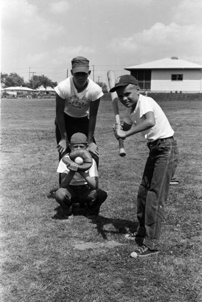 Michael "Mickey" Schepp stands at bat during a baseball game with catcher Dick Froemming and umpire Clarement Redders Jr. Ten-year-old Mickey, the son of Charles and Matilda Schepp, is featured because he had had surgery to correct a heart ailment and is now able to participate in sports with his twin brother, Richard (Ricky).