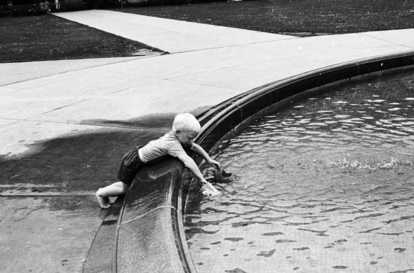 James, the three-year-old son of Philip and Mrs. Staudenraus, playing with a sprinkling can in the new University of Wisconsin library mall fountain.
