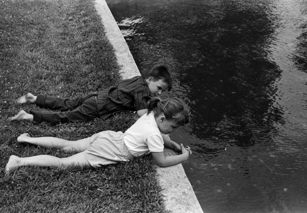 Six year old twins Billy and Martha Haygood lying in the grass next to a pond, looking down at trout fingerlings swimming at the fish hatchery located on Fish Hatchery Road. The photograph was taken as part of an article suggesting Madison places and activities for summertime visiting.