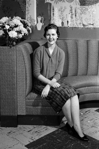 Nancy Miles models a skirt and sweater combination while sitting on a sofa.