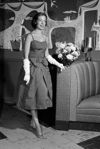 Stephanie Foster modeling a sable brown moire taffeta cocktail dress, styled with a bubble skirt and elbow length gloves.