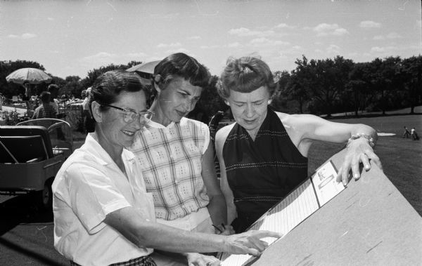 Checking the scoreboard are three of the low handicap 18 hole players at the annual Women's Interclub golf play between the women golfers of the three Madison private country clubs. Left to right, they include: Jay Purves of the Maple Bluff Country Club; Dorothy Golden, Nakoma; and Vera Roestiger, Blackhawk.