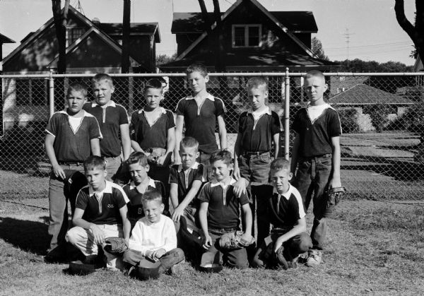 Group portrait of Badeau Plumbing's Midget baseball team, winners of the East Midget Central No. 3 championship. Batboy seated in front: Steve Badeau. Kneeling left to right: Gill Hamre, Craig Harbort, Steve Ely, Jim Krause, Bob Briggs. Standing left to right: John Meyers, Dale Tyggum, Steve Evert, Jeff Martell, Bob Badeau, Bill BonDurant.