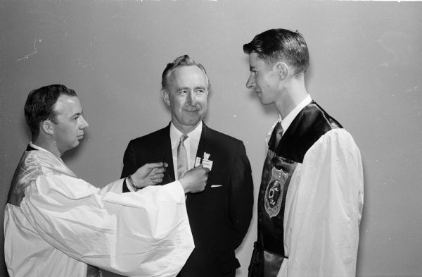 Initiation ceremony of the University of Wisconsin-Madison chapter of Alpha Kappa Psi professional business fraternity. Governor Vernon W. Thomson became Wisconsin's first governor to be initiated into the fraternity. Master of Rituals Charles Haas, Fond du Lac, left, initiates Gov. Thomson, center, at the honorary initiation. At right is John Borden, Elm Grove, president of the fraternity and master of ceremonies for the event.