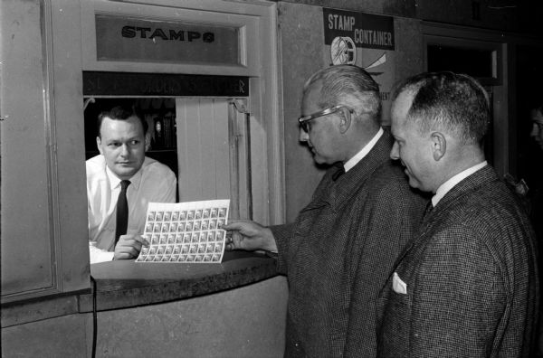 Wisconsin State Journal Editor Roy L. Matson buys stamps from Charles Smythe, wholesale stamp clerk, while Postmaster John F. Whitmore waits his turn. They were promoting buying stamps for Christmas cards early before the big mailing rush begins.