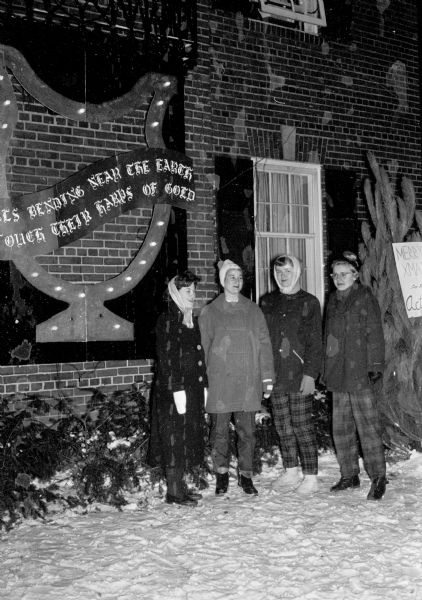 The front of the Alpha Chi Omega chapter house is decorated with a golden lyre Christmas decoration, put up as a surprise by the pledges. Pledges, left to right, are: Joan Avery, Mary Stouffer, Judy Adamson, and Maude Garness.