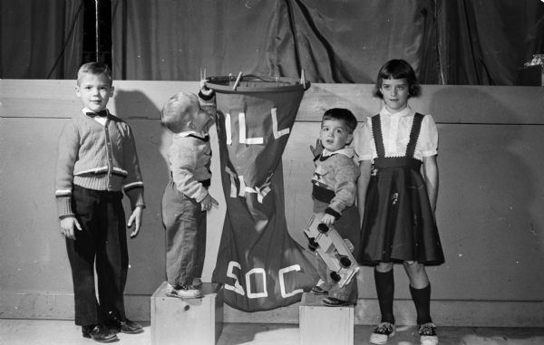 The Madison Twin Club held its Christmas Party at the Madison Community Center. Each child at the party presented a gift to the Empty Stocking Club. Standing by the Christmas stocking are (left to right) John Mackey, Jeffrey Mackey, James Mackey, and Janice Mackey. The children are the two sets of twins of Mr. and Mrs. J.M. Mackey.