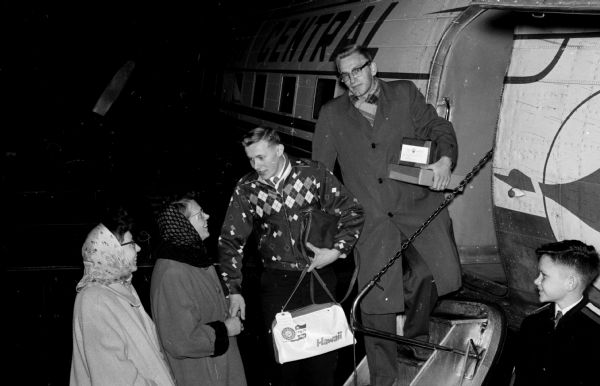 William Scobie, age 16 of Brodhead, holds a flight bag while embarking an airplane. Scobie won a trip to Hawaii for selling the most subscriptions to the <i>Wisconsin State Journal</i> in a contest held during November and December. He bids goodbye to his sisters, Mrs. Norman Everson and Mrs. Duane Youngblood. At the top of the steps is Frank Burkart, district circulation manager for Madison Newspapers, Inc.