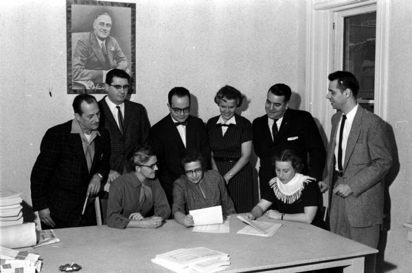 Committee chairmen for the Democratic Club of Dane County inauguration dinner & ceremony event check over last minute details. Shown seated (left to right) are Mrs. Marjorie Anderson, dinner tickets; Mrs. Elizabeth Tarkow, club chairman and director of local arrangement; and Mrs. Edwina Miller, coat checking. Shown standing (left to right) are B.M. (Bud) Morton, general arrangements; William Angus, sergeant-at-arms; John T. Howard, general arrangements; Mrs. Margaret Watrous, invitations; Stanley Prideaux, sergeant-at-arms; and James VanDeBogart, chairman of the banquet and ball.