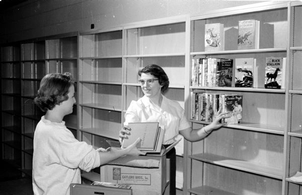 Shelves at the new Lakeview branch library at Troy and Northport Drives are being stacked in preparation for the library's grand opening. Mrs. Dianne Lee (left), library assistant, hands books to Mrs. Delores Brasch (right), acting branch librarian.