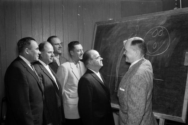 Joe Wilman (right), of the Brunswick Advisory Staff of Bowling Champions, diagrams a point during the school for bowling alley proprietors and managers as five men look on. The five men, left to right, are: Norb Pick, Prairie du Sac; Lyman Steve, Middleton; Al Hovland and Art Krueger, University of Wisconsin physical education instructors; and Bill Steele, Madison Plaza.