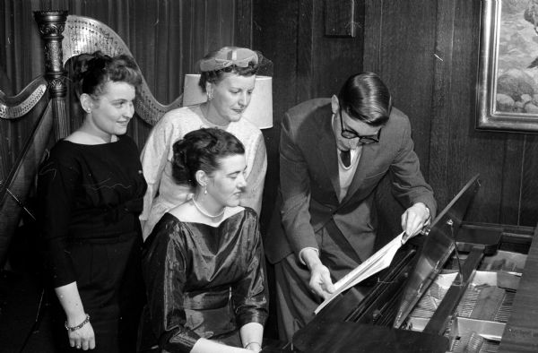 Charlotte Burr (left) and Margaret Wilber, standing, inspecting the musical program for the Sigma Alpha Iota Benefit Musicale. Seated is Nancy Becknell, and holding the music is Arthur Bohrs, both of whom accompanied the harp, flute and vocal artists. Proceeds from the concert are to go towards a scholarship for a woman student in the University of Wisconsin School of Music.