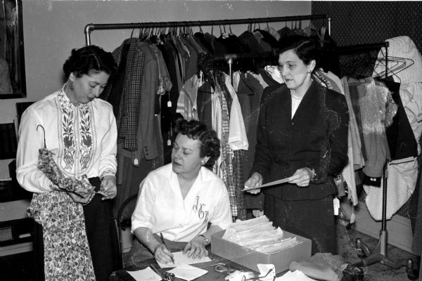 Three women are shown pricing re-sale clothing for a rummage sale at 110 West Washington Avenue. At work are, left to right: Imogene Bowers, Jane Brandt, and Geraldine Jacobson.