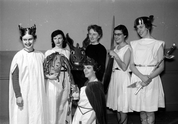 A scene from a variety show is put on by University of Wisconsin Dames Club units. Actresses in a comedy-tragedy, "Apologies to the Greeks", given by the Varsity Wives include, standing left to right: Mrs. Walter Luethy, Audrey Hinz, Nora Johnson, Rita Martens, and Mrs. Dallas Dollase. Kneeling in front is Mrs. Howard Savage.
