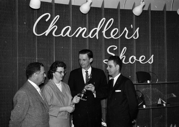 Joan Frey, a clerk at the Chandler Shoe Store, receives a national award for courtesy and cheerfulness from Richard Johnston, retail division manager of the Madison Chamber of Commerce. The award was made by the Edison Brothers Stores, Inc., of which Chandler's is a division. Looking on is David Glaser (left), regional manager of Chandler's stores and B.B. Barber, Chandler store manager.