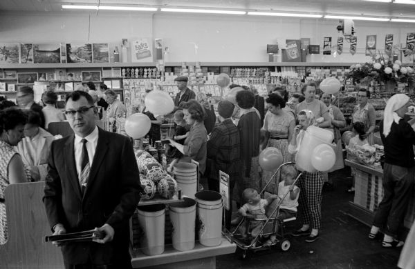 Robert Retzlaff (left), manager of the newly opened Ben Franklin variety store at 4204 Monona Drive, posing in the foreground on his store's first day of business. Merchandise and shoppers are behind him.