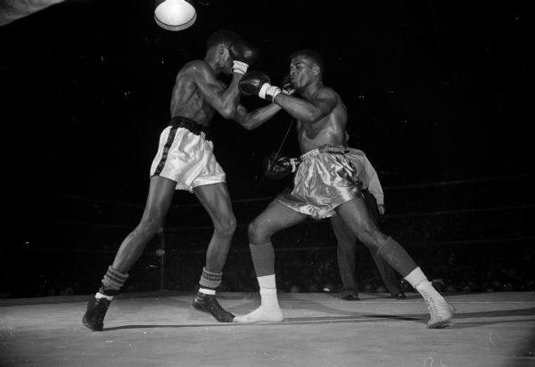 Cassius Clay (left), and Amos Johnson of the Marines spar during their match during the Pan American Games finals tournament at the University of Wisconsin field house. Johnson won in a split decision, snapping Clay's winning streak at 36, and preventing him from competing for the team in the competition in Chicago, subsequently motivating him to train harder at home in Louisville.