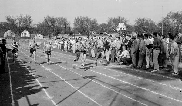 Four sprinters finish their race as spectators watch them go by. Sprinters and their order of finish are, left to right: Don Lautz, West (4) ;Dick Berens, Central (3); and Bill Smith, East (2).