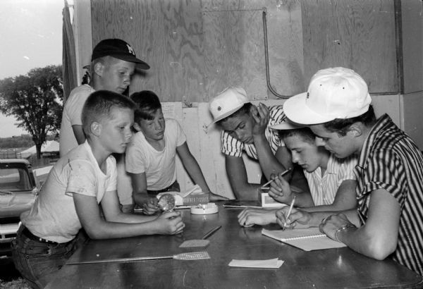 The 1959 Dane County Junior Fair is "home" for hundreds of 4-H Club members for four days. Registering 4-H members Steven, David, and Ted Olson, Rt. 3, Stoughton, shown on the left, are Mike Bradley, 814 Rutland Drive; Rodney Hustad, Rt. 4, Madison; and Jerry Johnson, 4205 Milwaukee Street, shown on the right.