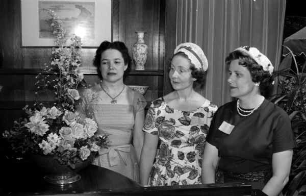 Three university faculty wives admire a floral arrangement at the University League tea to honor the wives of visiting summer session faculty members at the University of Wisconsin. Pictured are Mrs. Cynthia Youmans, Mrs. David Train of London, England, and Mrs. Genevieve Busse.