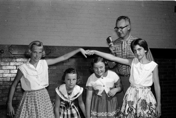 A dance called "The Green Sleeves" is being learned by four girls. Left to right are Mary Gjertson, 518 Maple Avenue; Mary Jane Frish, 2422 Coolidge Street; Barney Fry, 472 Togstad Glenn; and Susan Debs, 1315 Hoven Court.  The caller, standing in back, is John White, 118 Shepard Terrace, a YMCA member.