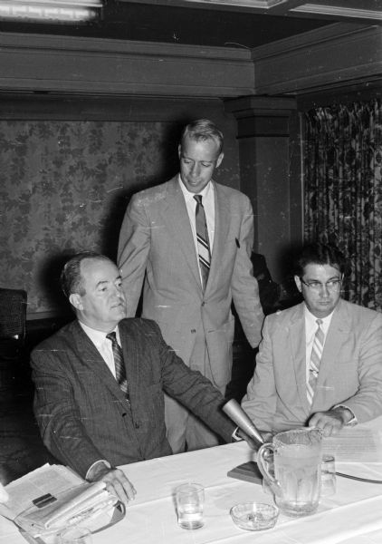 Senator Hubert Humphrey appears at a press conference at the Hotel Loraine. Shown (L-R) are Senator Humphrey, (standing) Assemblyman Fred Risser (D-Madison), and William Angus, vice-president of the Dane County Democratic Party.